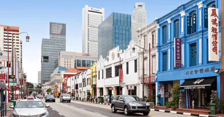 Row of colourful heritage shophouses on a Singapore street with office towers behind